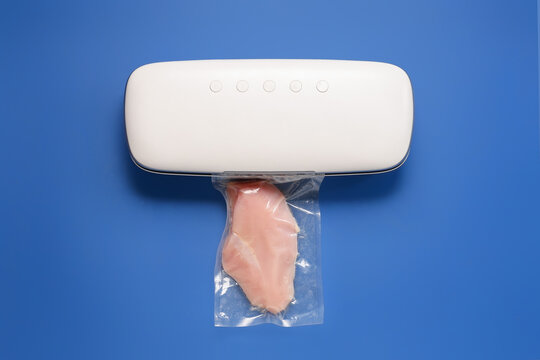 Vacuum sealer machine for food with chicken fillet in pack on blue background