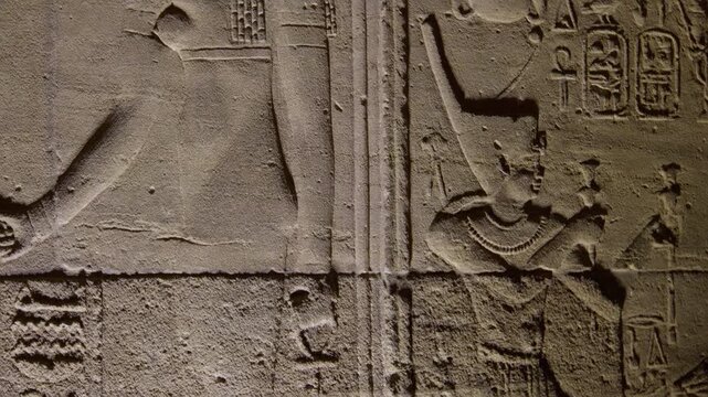 Close-up of ancient stone relief carving of goddess Isis with sun disc and cow horns crown inside Philae temple, Aswan, Egypt, surrounded by hieroglyphic inscriptions on sandstone wall.