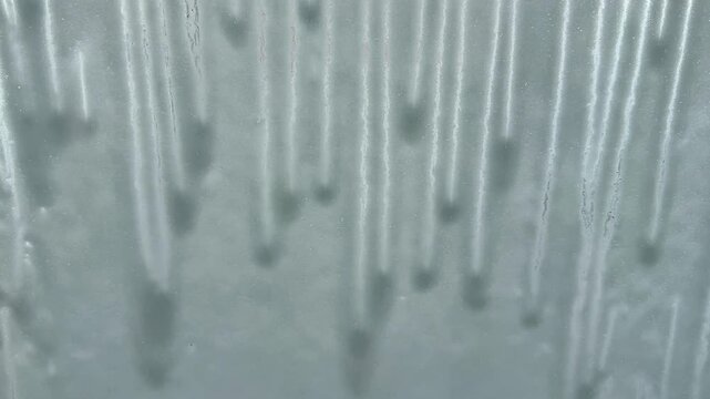 Foam sliding down car windshield during self service car wash. POV from inside vehicle showing active washing process with soap flowing and cleaning surface.