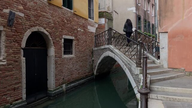Solitary Figure Crossing Stone Bridge Over Venetian Canal