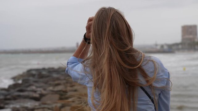 Woman with long hair standing by sea in windy coastal weather