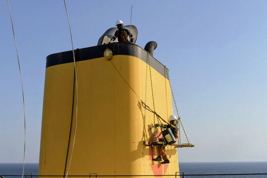 seafarers carrying out maintenance and painting work on ship funnel using rope access above open sea