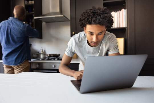 Teen boy using laptop for homework with father in the background