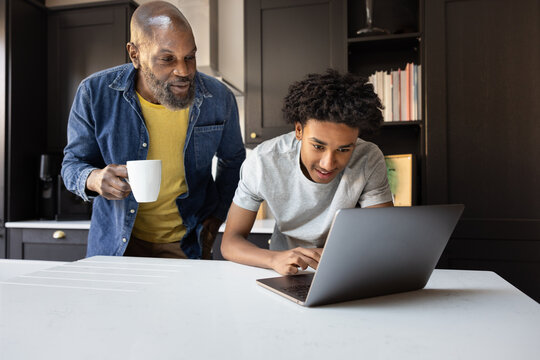 Father observing son on laptop with a coffee mug