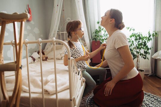 Daughter playing doctor with mother, crutches nearby