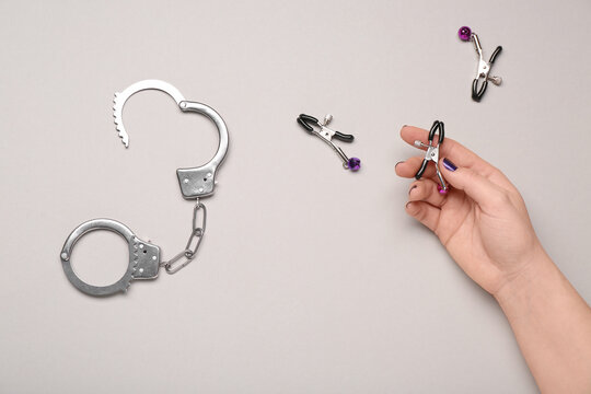 Female hand with handcuffs and nipple clamps from sex shop on light background