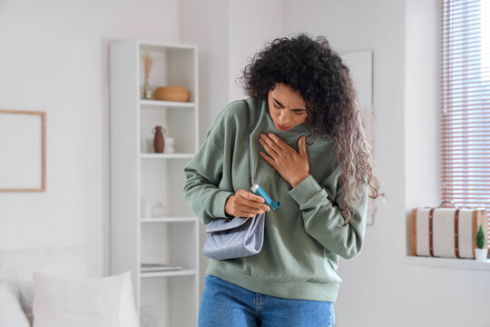 Young African-American woman with inhaler having asthma attack in bedroom