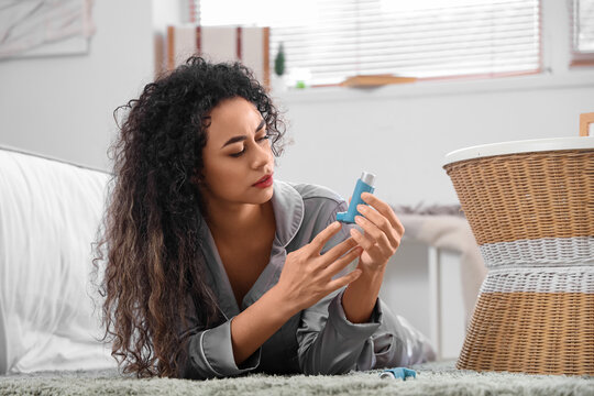 Young African-American woman with asthma inhaler lying on floor in bedroom