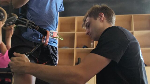 Trainer in gym securely tightens fastenings on clients legs. Experienced athlete helps checking newbies protective belts slow motion