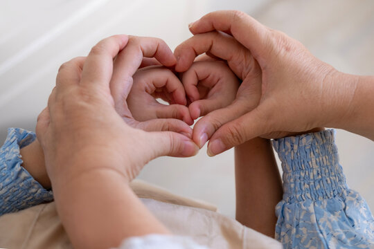 Grandmother, mother and daughter form heart with hands, intergenerational connection female generations, heartwarming image three generations women