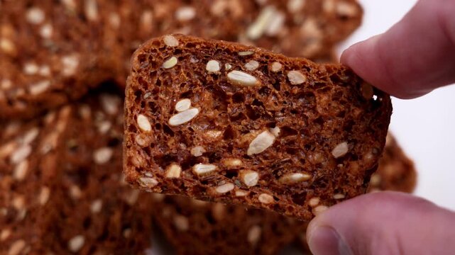 Hand holding multigrain whole grain crispbread slice. Close up of healthy toasted snack with seeds and grains. Crunchy baked texture