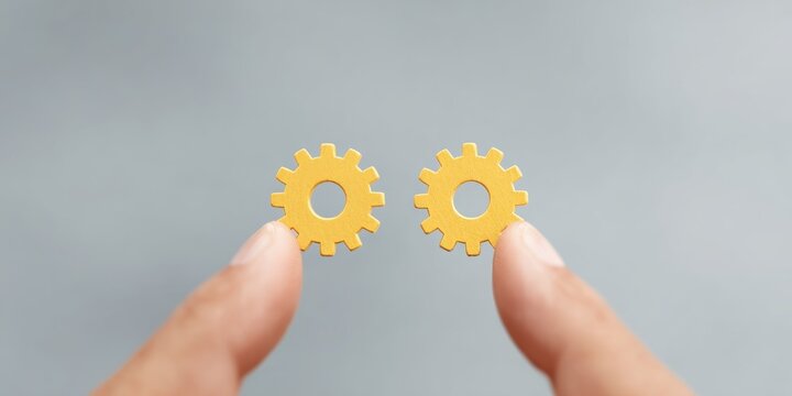 Hand holding two yellow gear wheels representing teamwork collaboration problem solving and synchronized business process efficiency concept
