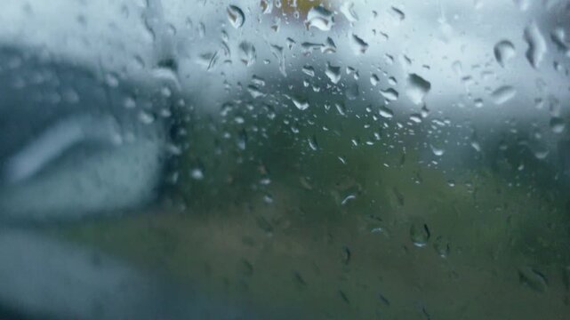 Raindrops falling on car window glass close up
