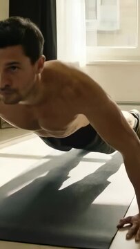 Vertical video: Starting shirtless man doing push-ups at home using dark mat, training for strength