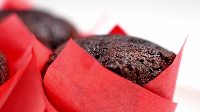 Person hand placing a dark chocolate muffin in a red paper wrapper on a white table. Concept of festive treat