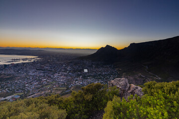 Fototapeta premium An iconic blue hour and dawn seen from Lion's head over the skyline of Cape Town in South Africa with views on the spectacular and iconic Table mountain and Devil's head, while the sky shows its colou