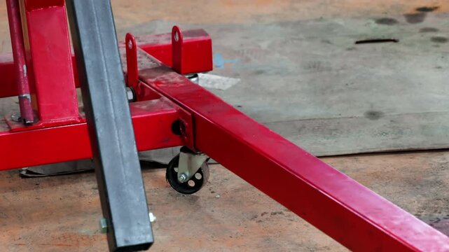 Mechanic in protective gloves services base of hydraulic crane. Man reviews lift small metal wheel before starting work process of engine restoration
