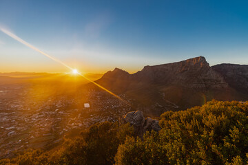 Obraz premium An iconic sunrise seen from Lion's head over the skyline of Cape Town in South Africa with views on the spectacular and iconic Table mountain and Devil's head, while the sun peaks just over the hills 