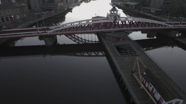 Predawn aerial view in Newcastle showing the red Swing Bridge reflected in the River Tyne, with the Gateshead Millennium Bridge and The Glasshouse silhouetted in the background.