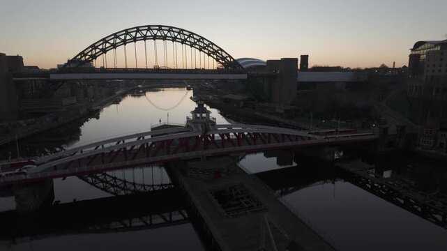 Predawn aerial view of the Newcastle quayside featuring the Swing Bridge and Tyne Bridge reflected in the still water, with The Glasshouse and Millennium Bridge in the background.
