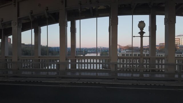 View from the High Level Bridge in Newcastle looking west at dawn, framing the River Tyne and distant Metro Bridge through historic iron pillars.

