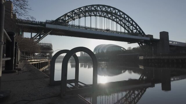 Cinematic low-level slide along the Newcastle quayside at dawn, featuring the iconic Tyne Bridge with the Glasshouse (Sage) and Millennium Bridge reflected in the river.