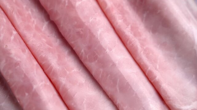 Fresh thin slices of cooked ham. Pink deli meat folded in a row. High-protein breakfast ingredient. Rotation