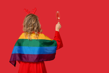 Young woman in reindeer horns with LGBT flag and glass of champagne on red background. Christmas celebration © Pixel-Shot