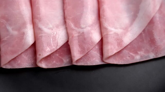 Thinly sliced cooked ham arranged in folds on dark surface. Processed pork deli meat. Ready to eat product. Rotation