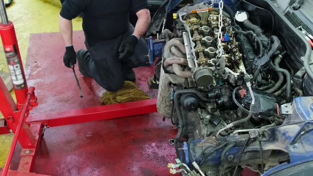 Specialist repairs major part of vehicle during shift. Special chains of crane hold engine above workshop floor during repair process