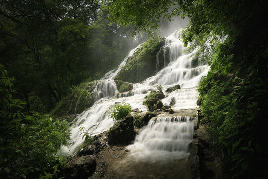 Waterfall cascading down cliffs in a moody dark forest. A dreamy landscape with mist and majestic beauty.