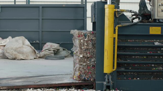 Industrial baler machine creating a dense cube of recycled plastic waste at a processing plant