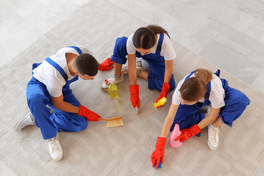 Team of young janitors cleaning carpet in room, top view