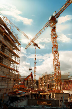 Construction site with yellow cranes looming into the blue sky with dramatic clouds. Wide angle tilted up view. 