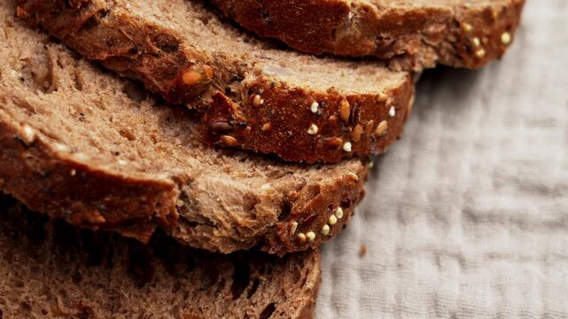 Stack of sliced dark German bread with seeds on rustic fabric background. Crispy crust and dense whole grain crumb. Traditional baking style. Concept of artisanal bakery. Rotation