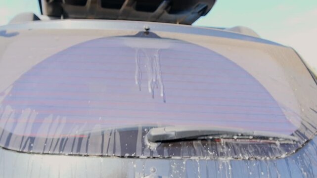 SUV rear window wiper operating with washer fluid spraying and clearing dirty glass, close-up view of Car cleaning process, visibility improvement, automotive maintenance, safety driving feature