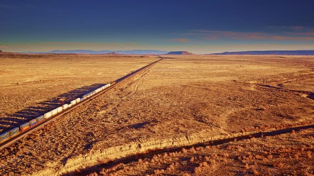 Wide drone shot freight train traveling through western mountains and plains, rail transport, logistics network