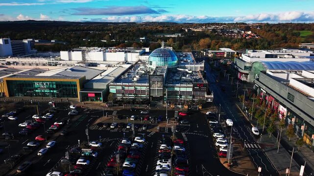 Aerial drone footage showing Livingston Designer Outlet shopping centre during the day with retail buildings, car park, and surrounding urban area in Livingston, Scotland