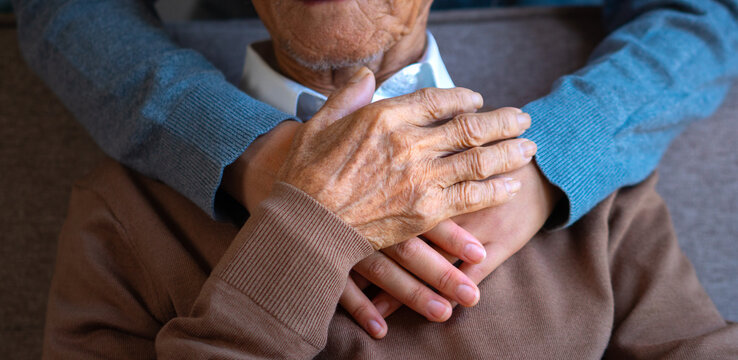 A close-up image of a caregiver's hands comforting an elderly man in a home-based care facility reflects the concept of caring for and assisting the elderly.