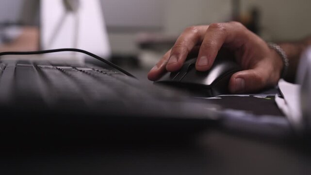 a hand typing on a keyboard at a modern office desk beside a computer mouse, captured indoors with soft light and shallow depth of field.
