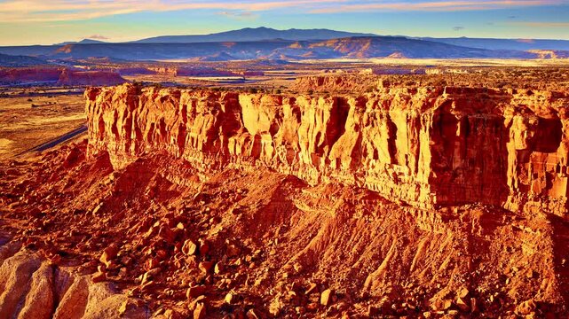 Cinematic aerial retreat from a red rock mesa unveiling a vibrant sunset-lit rock face in New Mexico