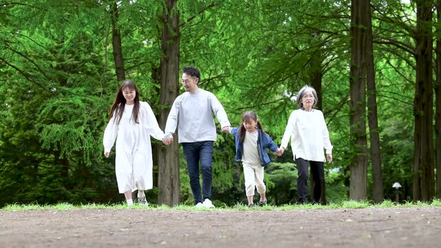 A three-generation family enjoying a walk in a park with fresh greenery: A video capturing their happy family life in slow motion, full-body shot