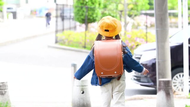 ランドセルを背負って道路の横断歩道を渡ろうとする小学生の後ろ姿、車は危険だよ～事故防止の飛び出し禁止、登校や通学の交通安全イメージ　顔無しの動画