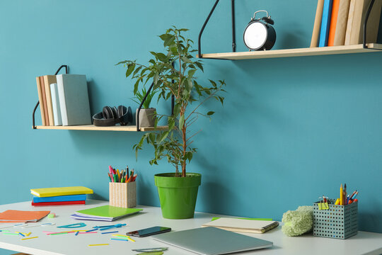 Modern school desk with stationery in room near blue wall