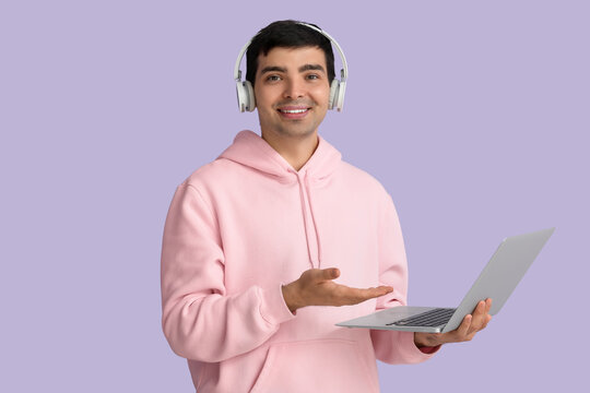 Male programmer in headphones with laptop on lilac background
