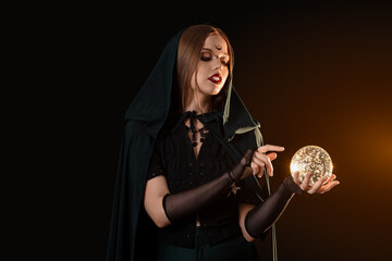 Fototapeta premium Beautiful young witch with crystal ball on dark background