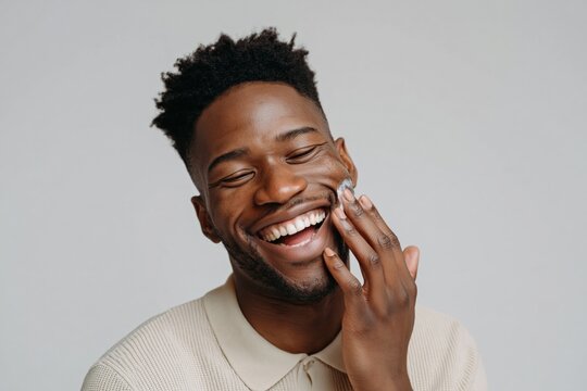 Male model applying moisturizer with joyful smile in studio