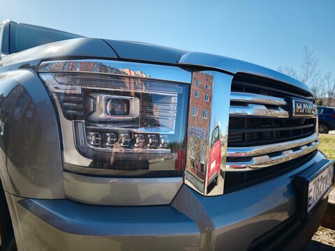 Sosnoviy Bor, Russia - March 24, 2026: Haval H6 front view showcasing chrome grille and LED headlights with reflections of buildings in the background under clear blue sky