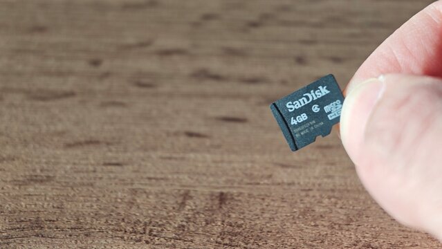 Sosnoviy Bor, Russia - April 21, 2026: Hand holding a SanDisk 4GB microSD card against a wooden surface, showcasing storage capacity and brand details clearly visible
