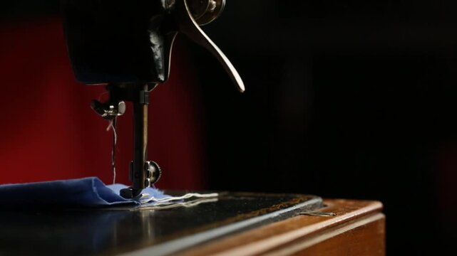 A seamstress works on a vintage black sewing machine, space for text, sewing blue fabric